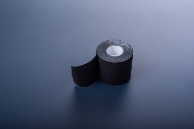 Tıbbi kaset siyah bir arka plan üzerinde yatıyor. Siyah rulo kineziotape. Yama yaralanmalar ve eklem kronik hastalıklar için sporcular tarafından kullanılır. Yatay.