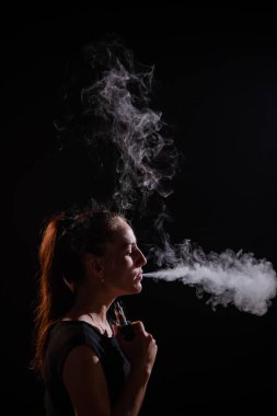 Esmer, siyah arka planda elektronik bir sigara içiyor ve ağzından yoğun bir duman salıyor. Bir kadın portresi sigara içiyor, havada süzülüyor..