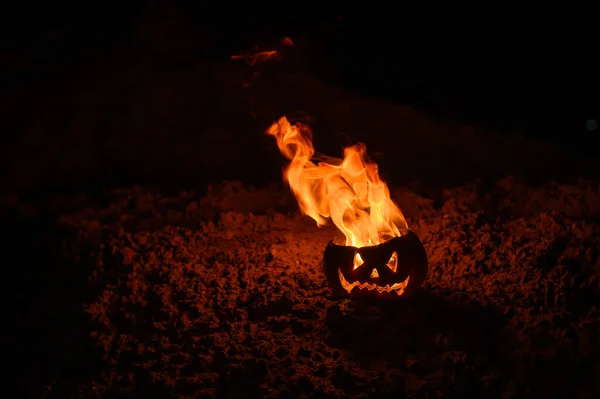 Językami płomienia w dyni. Jack-o-Latarnia w ogniu na czarnym tle. Halloweenowy symbol na ziemi. Cukierek albo psikus. Zbliżenie. — Zdjęcie stockowe