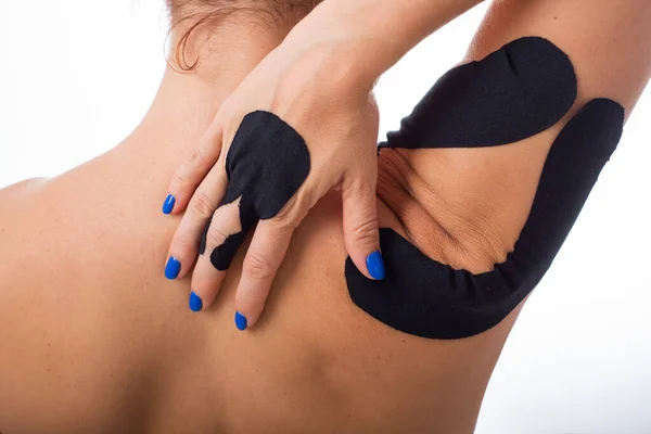 Vrouwelijke schouder met kineziotape op een witte achtergrond. Alternatieve geneeskunde voor sportblessures van gewrichten en ligamenten. Jonge Sportvrouw met een zwarte medische taping op een zere schouder en vinger. — Stockfoto