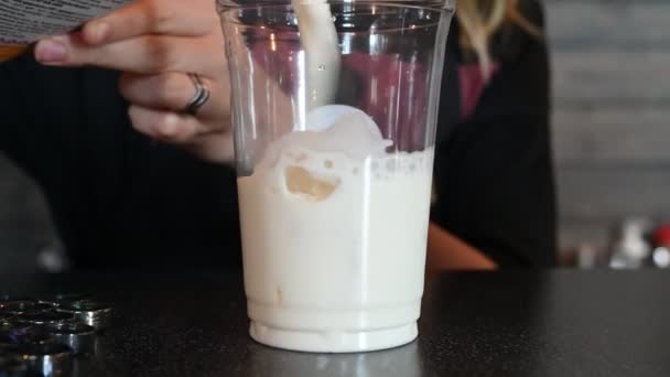 Il barman versa la panna in un cocktail di caffè. Il barista versa il latte in un bicchiere di plastica con ghiaccio, preparando il caffè freddo. Un rinfrescante drink da asporto estivo . — Video Stock