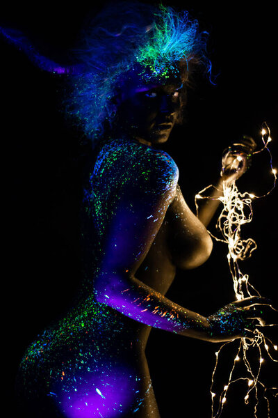 Devil makeup. Beautiful woman in profile in ultraviolet body art, glows in the dark. Girl is painted in fluorescent powder