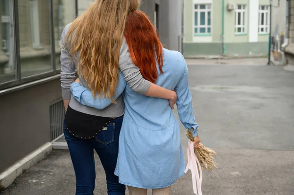 同性の関係幸せなレズビアンのカップルが通りを歩き、腰の周りに優しく抱き合いました。ドライフラワーの花束を持つデートに2人の美しい女性の背中。Lgbt. — ストック写真