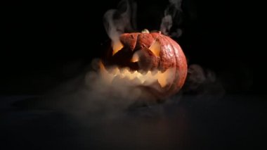 Cadılar Bayramı, karanlıkta parlayan korkunç yüzlü turuncu balkabağı. Kalın gri duman çıkar ve siyah masaya yayılır. Tüm azizlerin arifesinde yanıp sönen bir el fenerinin yakın çekimi..