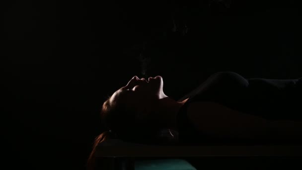 Брюнетка курить електронну сигарету на чорному тлі, вивільняючи густий дим з рота. Портрет жінки, яка курить вейп, що нависає . — стокове відео