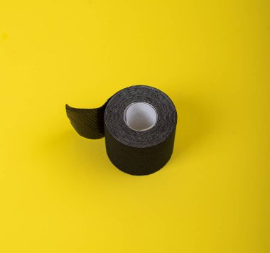 Tıbbi kaset sarı bir arka plan üzerinde yatıyor. Siyah rulo kineziotape. Kasları, eklemleri ve lenf drenajını desteklemek için tasarlanmış bir spor yama.