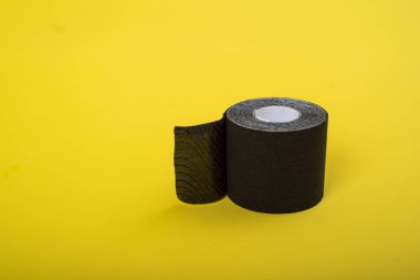 Tıbbi kaset sarı bir arka plan üzerinde yatıyor. Siyah rulo kineziotape. Kasları, eklemleri ve lenf drenajını desteklemek için tasarlanmış bir spor yama.