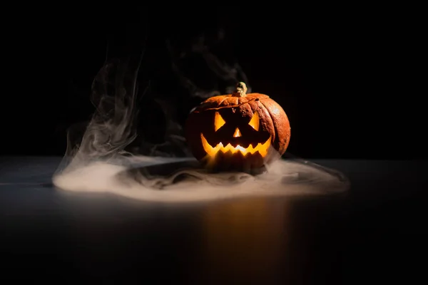Halloween, orange pumpa med en skrämmande lysande ansikte på en mörk bakgrund. Grå tjock rök kommer ut. — Stockfoto