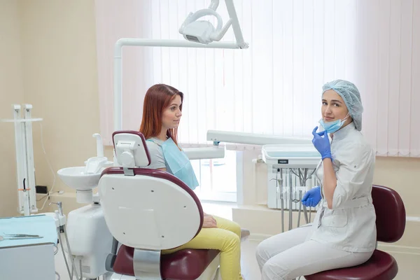 Una dentista e una paziente dai capelli rossi in uno studio dopo il trattamento dentale stanno guardando la fotocamera con facce felici. Donna felice con il suo medico dopo aver preso spettacoli. Servizi dentistici . — Foto Stock