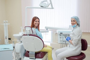 Bir kadın diş hekimi ve diş tedavisi sonrası bir ofiste kızıl saçlı hasta mutlu yüzleri ile kameraya bakıyor. Mutlu kadın, gösterileri aldıktan sonra doktoruyla birlikte. Diş hizmetleri. 