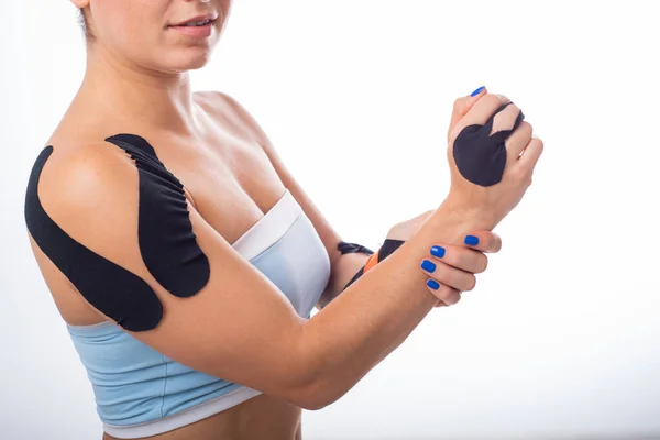 Female shoulder with kineziotape on a white background. Alternative medicine for sports injuries of joints and ligaments. Sportswoman with a black medical record on a sore shoulder and middle finger.