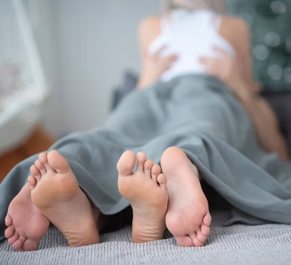 Gros plan des jambes masculines et féminines. Le couple aimant se couche et s'embrasse sur le lit sous une couverture grise. Salle lumineuse . — Photo