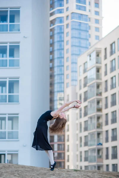 Ballerina v Tutu pózováním u vícepodlažní obytné budovy. Krásná mladá žena v černých šatech a špičkách bot s neuvěřitelnou flexibilitou. Nádherná baletka provádí elegantní beatový. — Stock fotografie