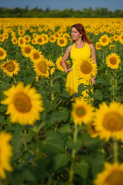 Eine rothaarige Frau in einem gelben Kleid steht auf einem Sonnenblumenfeld. schöne Mädchen im Rock Sonne genießt einen wolkenlosen Tag auf dem Land. rosa Haarsträhnen. — Stockfoto