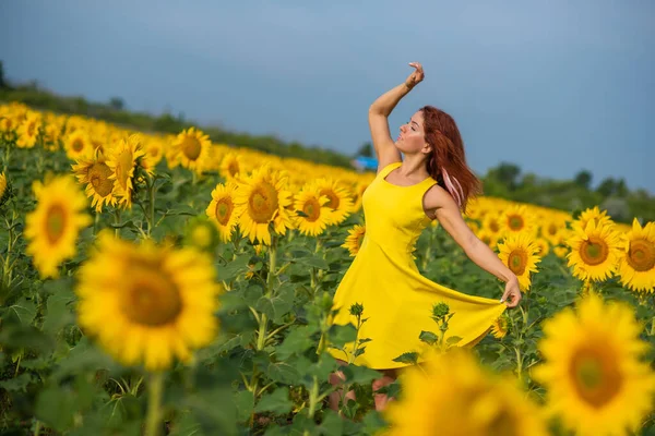 Eine rothaarige Frau in einem gelben Kleid steht auf einem Sonnenblumenfeld. schöne Mädchen im Rock Sonne genießt einen wolkenlosen Tag auf dem Land. rosa Haarsträhnen. — Stockfoto