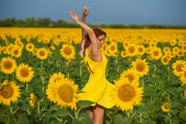 Eine rothaarige Frau in einem gelben Kleid steht auf einem Sonnenblumenfeld. schöne Mädchen im Rock Sonne genießt einen wolkenlosen Tag auf dem Land. rosa Haarsträhnen. — Stockfoto