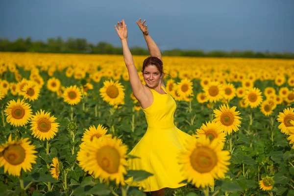 Rothaarige Frau in einem gelben Kleid, die mit erhobenen Händen in einem Sonnenblumenfeld tanzt. schöne Mädchen im Rock Sonne genießt einen wolkenlosen Tag auf dem Land. rosa Haarsträhnen. — Stockfoto