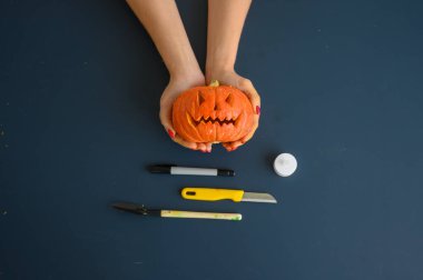  Kadın siyah arka plan üzerinde küçük bir kabak tutar. Cadılar Bayramı konsepti, düz yatıyordu, üst görünüm. Siyah bir masa üzerinde elinde mum, kalem, bıçak ve kabak.