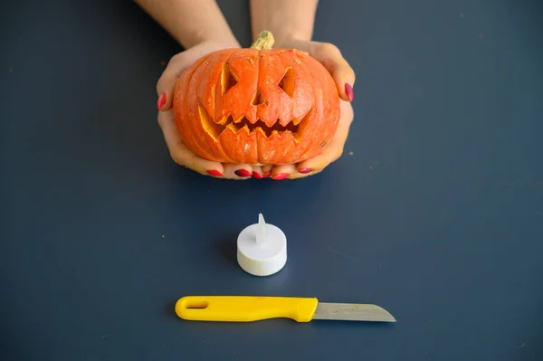 Frau hält einen kleinen Kürbis über schwarzem Hintergrund. Halloween-Konzept, flache Lage, Draufsicht. Kerze, Messer und Kürbis in der Hand auf einem schwarzen Tisch. — Stockfoto