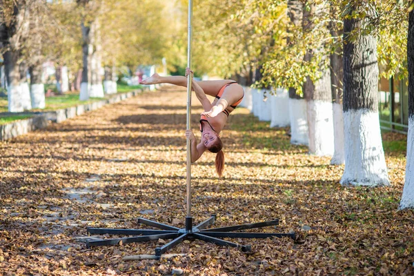 Belle gymnaste faire des tours sur une plate-forme portable dans un beau parc d'automne. femme danse sur une scène de poteau portable sur fond de chute de feuilles d'automne. Pole dance. Une danse étonnante — Photo