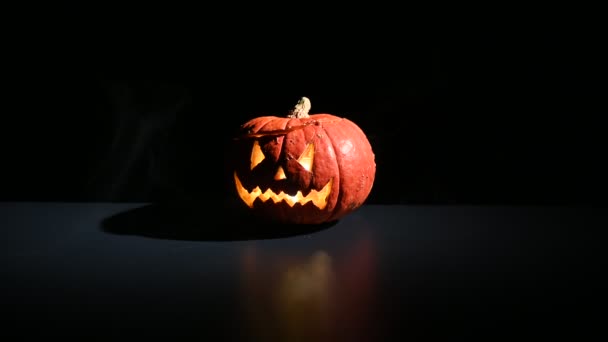 Halloween, orangefarbener Kürbis mit einem beängstigend leuchtenden Gesicht auf dunklem Hintergrund. Dicker grauer Rauch steigt auf. — Stockvideo