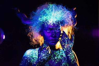 şeytan makyaj ve kontakt lensler. Ultraviyole vücut boyama kadın. Kız floresan tozuyla boyanmış. Uv ışıkta parlayan vücut sanatı. Gözlerindeki yıldızlar.