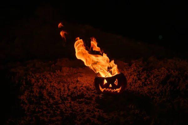 Tongen van vlam in een pompoen. Jack-o-lantern in brand op een zwarte achtergrond. Halloween symbool op de grond. Truc of behandelen. Close-up. — Stockfoto