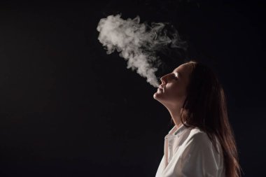 Beyaz gömlekli dalgın esmer karanlıkta nargile içiyor. Bir kadın portresi sigara içiyor, havada asılı duruyor. Siyah arka plan. Elektronik Sigara mı? Kötü alışkanlık..