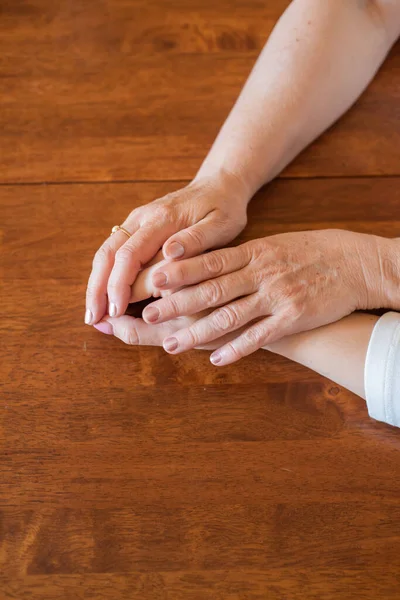 Elderly mother and her daughter holding hands while sitting at the table.Close up on women of different generations holding hands. Close Up Shot Of Mother And Daughters Hands Holding — Stock Photo, Image