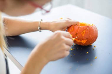 Bir kadın Cadılar Bayramı için bir balkabağına kötü bir somurtmayı kağıt bıçağıyla oyuyor. Tüm azizlerin arifesinde siyah bir masanın üzerinde kadın eli fener yapıyor..