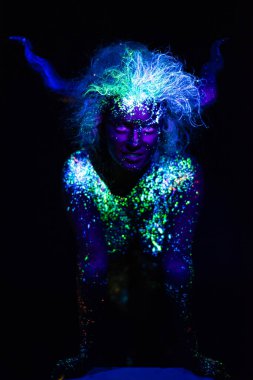 şeytan makyaj ve kontakt lensler. Ultraviyole vücut boyama kadın. Kız floresan tozuyla boyanmış. Uv ışıkta parlayan vücut sanatı. Gözlerindeki yıldızlar.