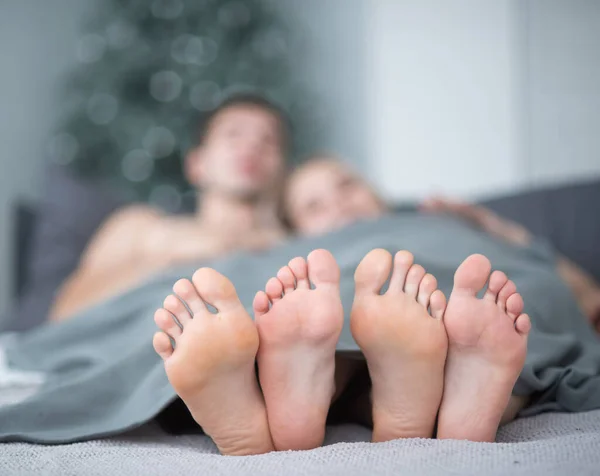 Närbild på manliga och kvinnliga ben. Den kärleksfulla paret ligger och omfamnar på sängen under en grå filt. Ljust rum. — Stockfoto