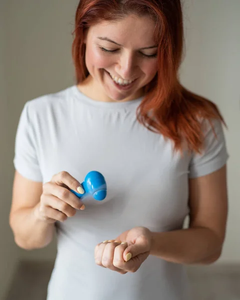 Menina ruiva seca esmalte com um ventilador de bolso. Uma mulher inventiva faz-se uma manicura em sua própria casa. Pequeno ventilador. Mulher feliz soprando em uma manicure brilhante pelo fluxo de ar . — Fotografia de Stock