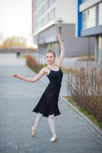 Bailarina en un tutú posando sobre el telón de fondo de un edificio residencial. Hermosa mujer joven en vestido negro y zapatos puntiagudos bailando ballet afuera . —  Fotos de Stock