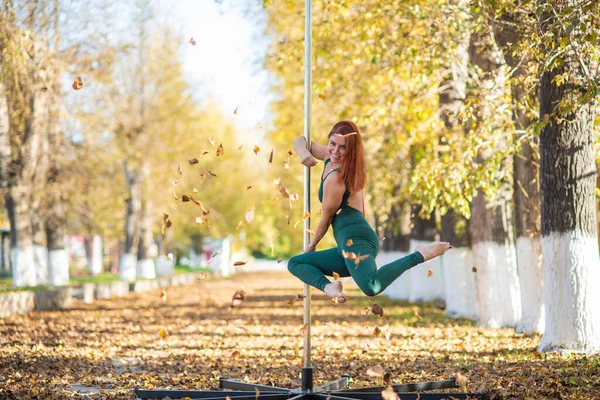 美しい体育館は美しい秋の公園のポータブルプラットフォームでトリックを行います。秋の紅葉を背景にポータブルポールステージで踊る女性。ポールダンスだ。素晴らしいダンスだ — ストック写真