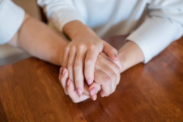 Elderly mother and her daughter holding hands while sitting at the table.Close up on women of different generations holding hands. Close Up Shot Of Mother And Daughters Hands Holding — Stock Photo, Image