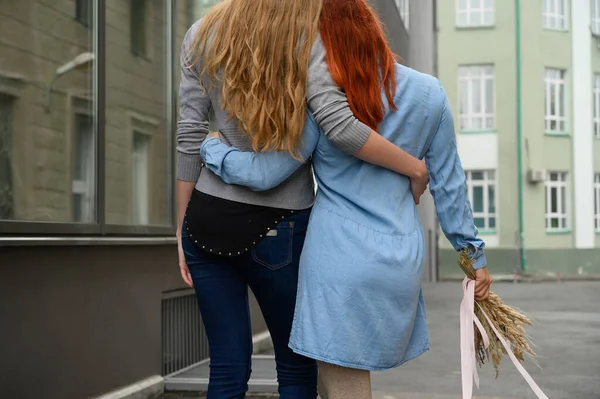 Relaties met hetzelfde geslacht. Een gelukkig lesbisch paar liep langs de straat en knuffelen zachtjes elkaar rond de taille. De rug van twee mooie vrouwen op een datum met een boeket van gedroogde bloemen. Lgbt. — Stockfoto