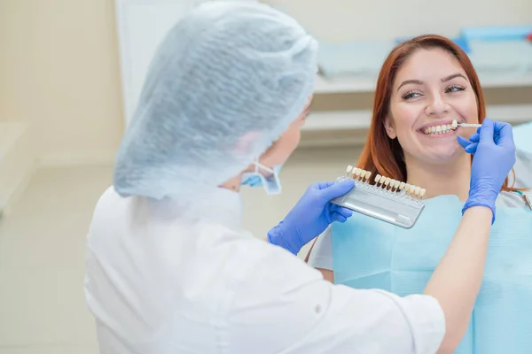 Перевірте і виберіть колір зубів у стоматологічному кріслі. Стоматолог робить процес лікування красивої молодої рудої дівчини. Вибір зубної імплантації . — стокове фото