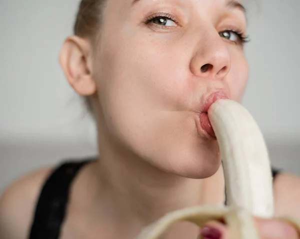Close-up do rosto, lábios, língua de uma jovem, menina europeia lambendo uma grande banana amarela, doce . — Fotografia de Stock