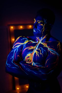 Ultraviyole desenli vücut sanatı bir erkeğin vücudunda dolaşım sistemi. Kaslı bir atletin gövdesinde, damarlar ve arterler floresan boyalarla çizilir. Beden geliştirici elinde lambalarla aynanın karşısında duruyor..