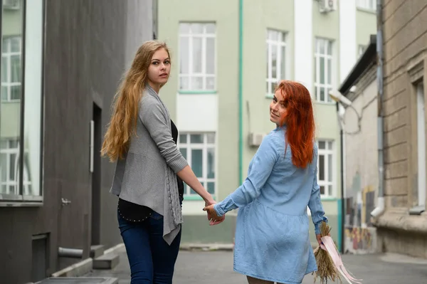 Relaciones del mismo sexo. Feliz pareja de lesbianas caminando por la calle tomados de la mano. Las espaldas de dos hermosas mujeres en una cita con un ramo de flores secas. LGTB . — Foto de Stock