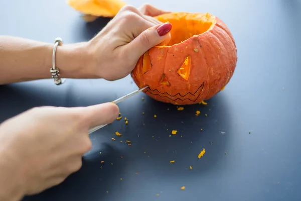 Una donna incide il viso su una zucca per una lampada di Halloween su un tavolo nero. Primo piano mani femminili che fanno Jack-o-lanterna alla vigilia di tutti i santi .. — Foto Stock