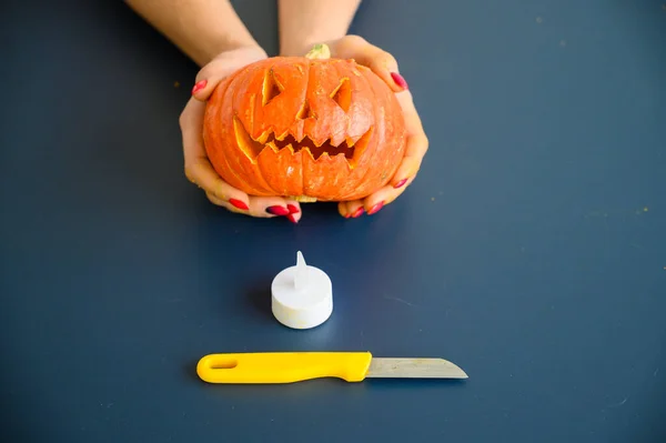 Frau hält einen kleinen Kürbis über schwarzem Hintergrund. Halloween-Konzept, flache Lage, Draufsicht. Kerze, Messer und Kürbis in der Hand auf einem schwarzen Tisch. — Stockfoto