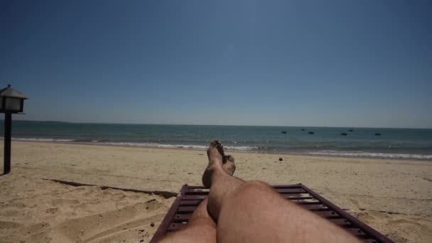 Piernas de macho peludo en la tumbona de la playa. Vista en primera persona de la playa y el mar en el horizonte . — Vídeos de Stock