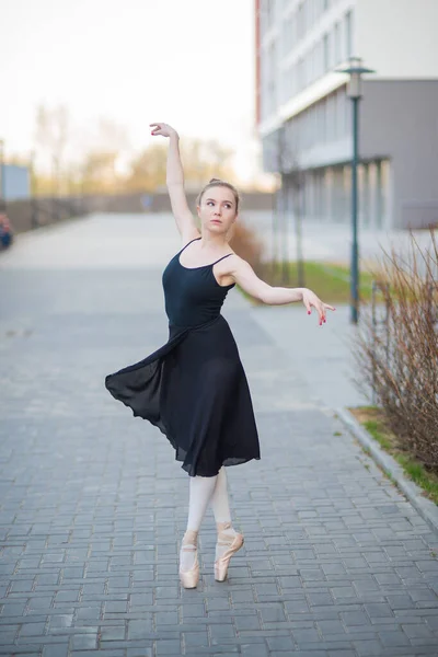 Ballerina in a tutu posing against the backdrop of a residential building. Beautiful young woman in black dress and pointe shoes dancing ballet outside. Elegant classical dance — Stock Photo, Image