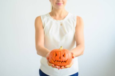 Beyaz bluz giymiş bir kadın Cadılar Bayramı için balkabağı tutuyor. All Saints arifesinde beyaz bir arka plan üzerinde bir fener jakı ile kadın ellerin yakın çekim. Ön plan. Hediye ver yoksa karışmam. Korkunç grimace.