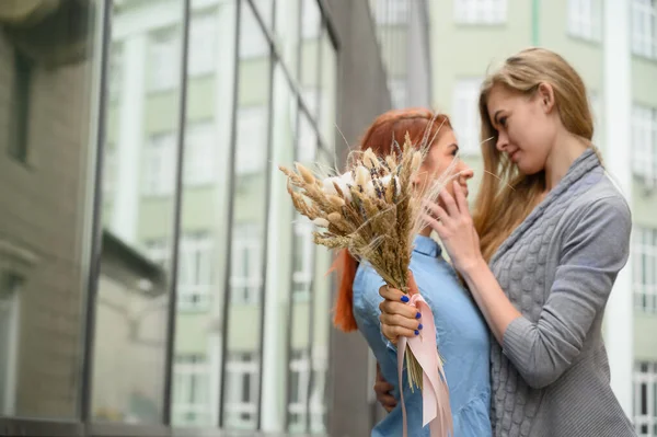 Relaciones del mismo sexo. Feliz pareja lesbiana con flores secas. Dos hermosas mujeres se abrazan tiernamente en una cita. Ramo en primer plano. Cerca de un par de manos.LGBT . — Foto de Stock