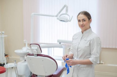 Beyaz üniformalı çekici kadın doktor eldiven giyiyor. Genç güzel kadın diş hekimi esmer eldiven giyen sandalye tarafından ofiste.