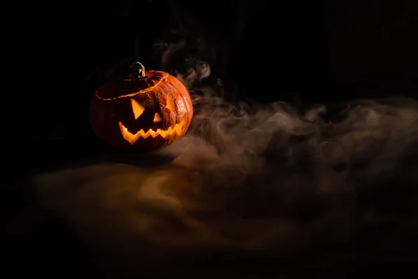 Halloween, apelsin pumpa med en skrämmande lysande ansikte på en mörk bakgrund. Tjock grå rök kommer ut och sprider sig över det svarta bordet. En närbild på en ficklampa. Dekorerat ljus stativ. — Stockfoto