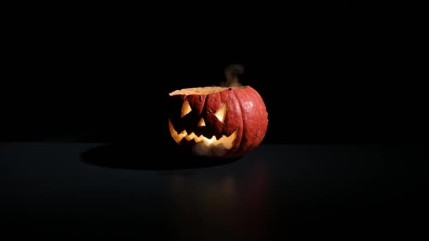 Хэллоуин, оранжевая тыква со страшным светящимся лицом на темном фоне. Толстый серый дым выходит и распространяется на черном столе. Крупный план фонарика без крышки накануне всех святых — стоковое видео